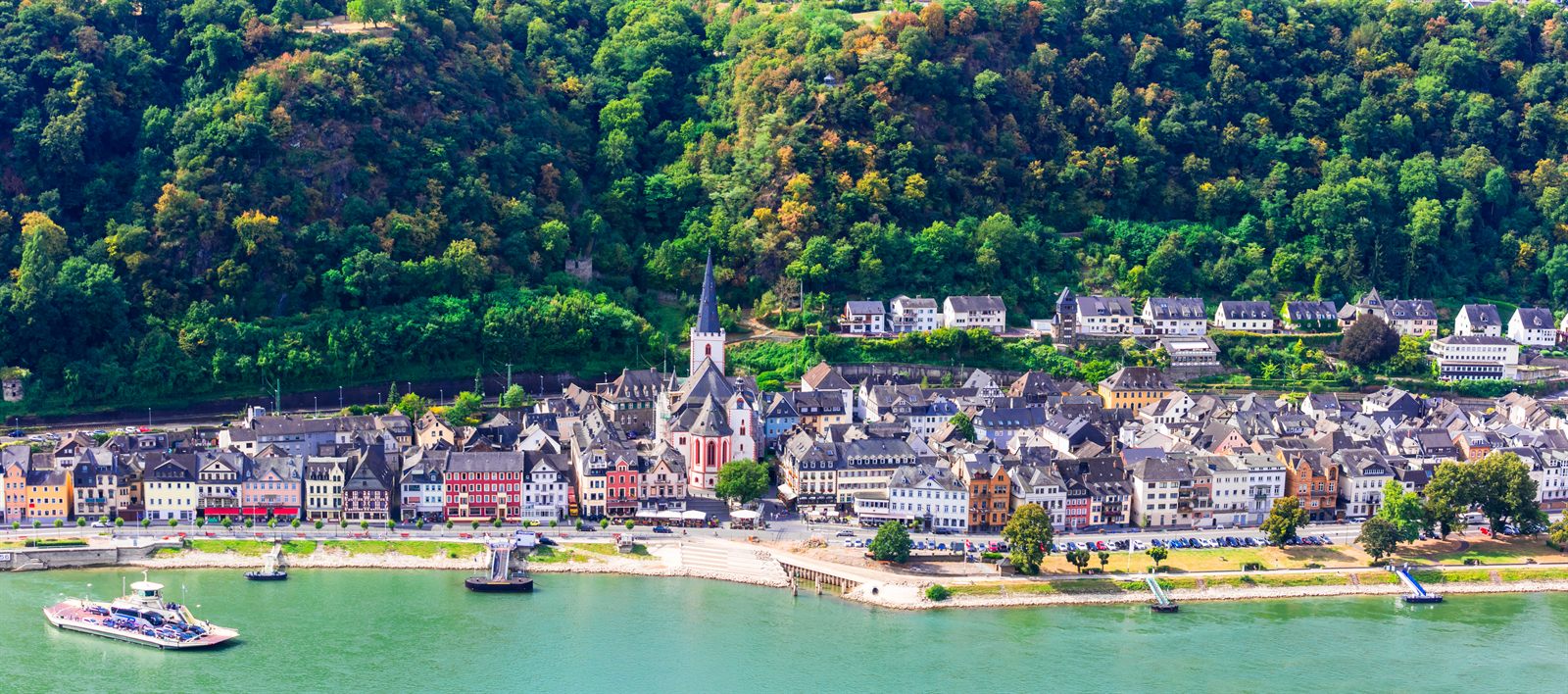 Rhine village below wooded hills with a cruise boat